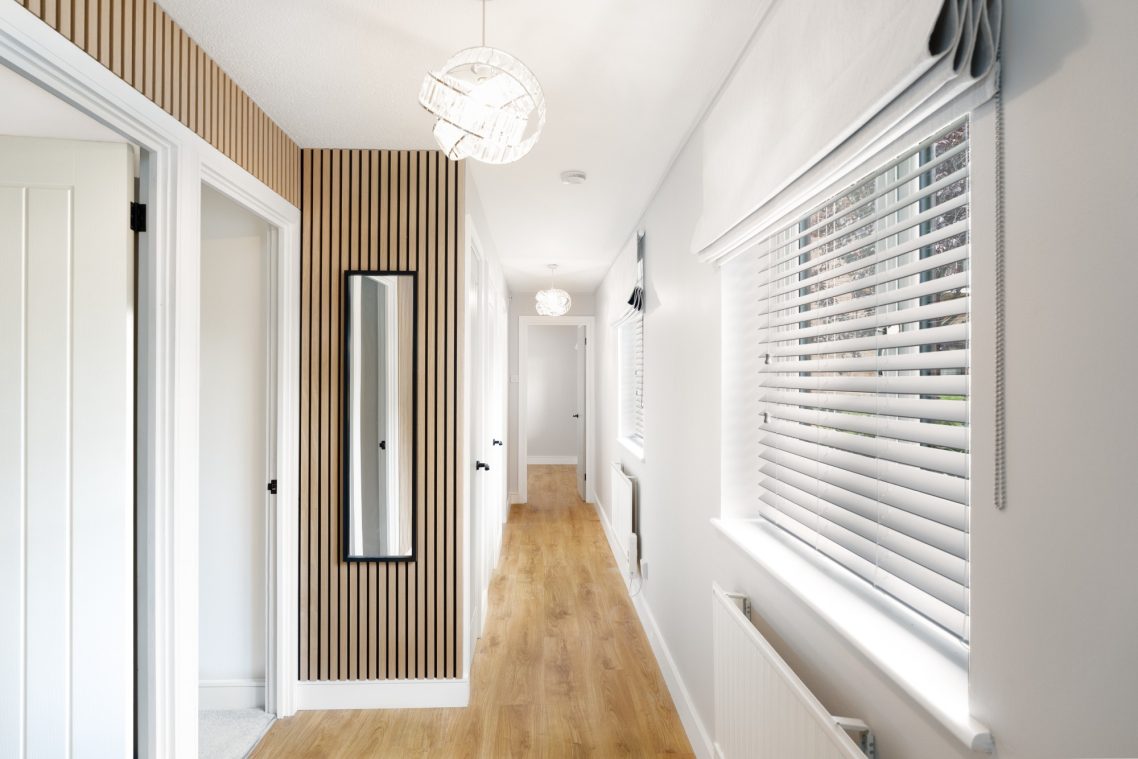 Bright corridor featuring wooden flooring, a mirror, and modern lighting.