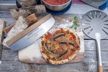 A pizza topped with herbs and vegetables, alongside a wooden pizza peel and ingredients.