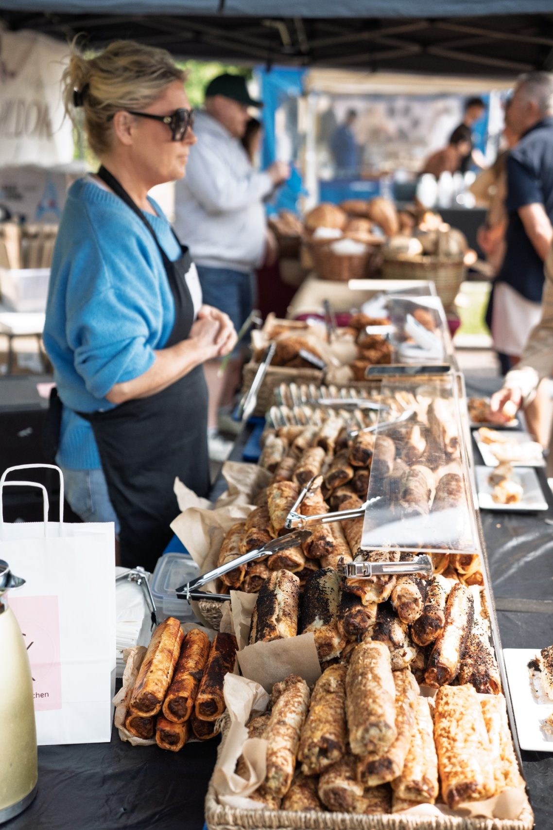 Vendor at a market stall selling various pastries and snacks.