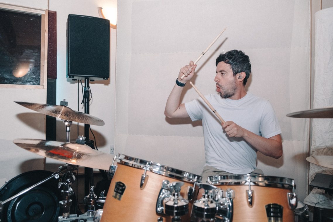 A man playing drums, focused, in a music studio setting.