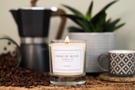 Coffee beans surround a lit candle, a plant, and a coffee maker on a countertop.