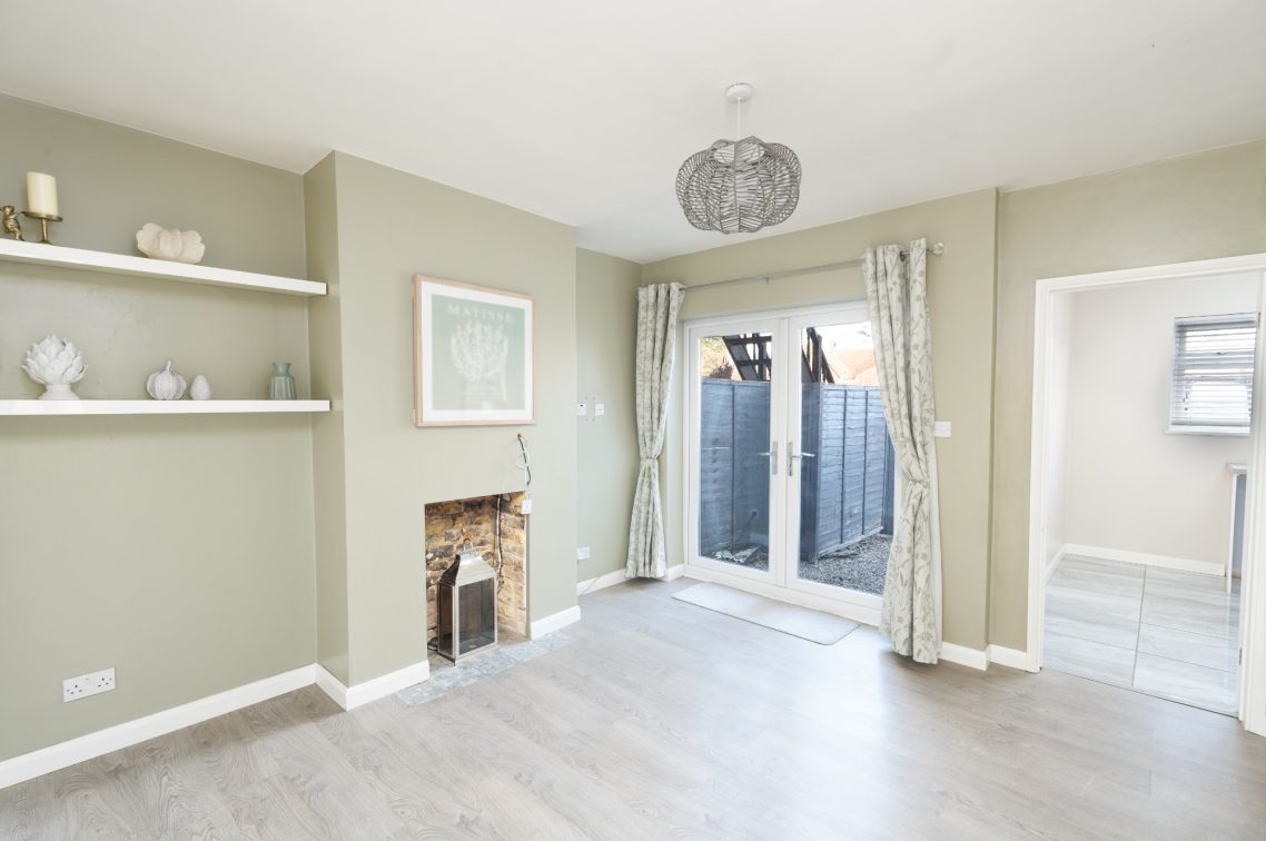 Light, airy room with pale green walls, wooden flooring, and doors leading to an outdoor space.