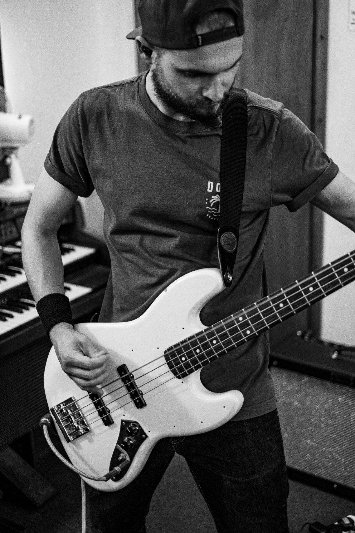 A musician playing a white bass guitar, focused on their performance in a studio setting.