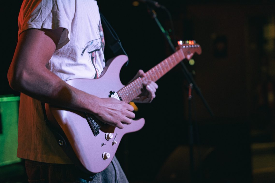 Person playing a pale pink electric guitar on stage.