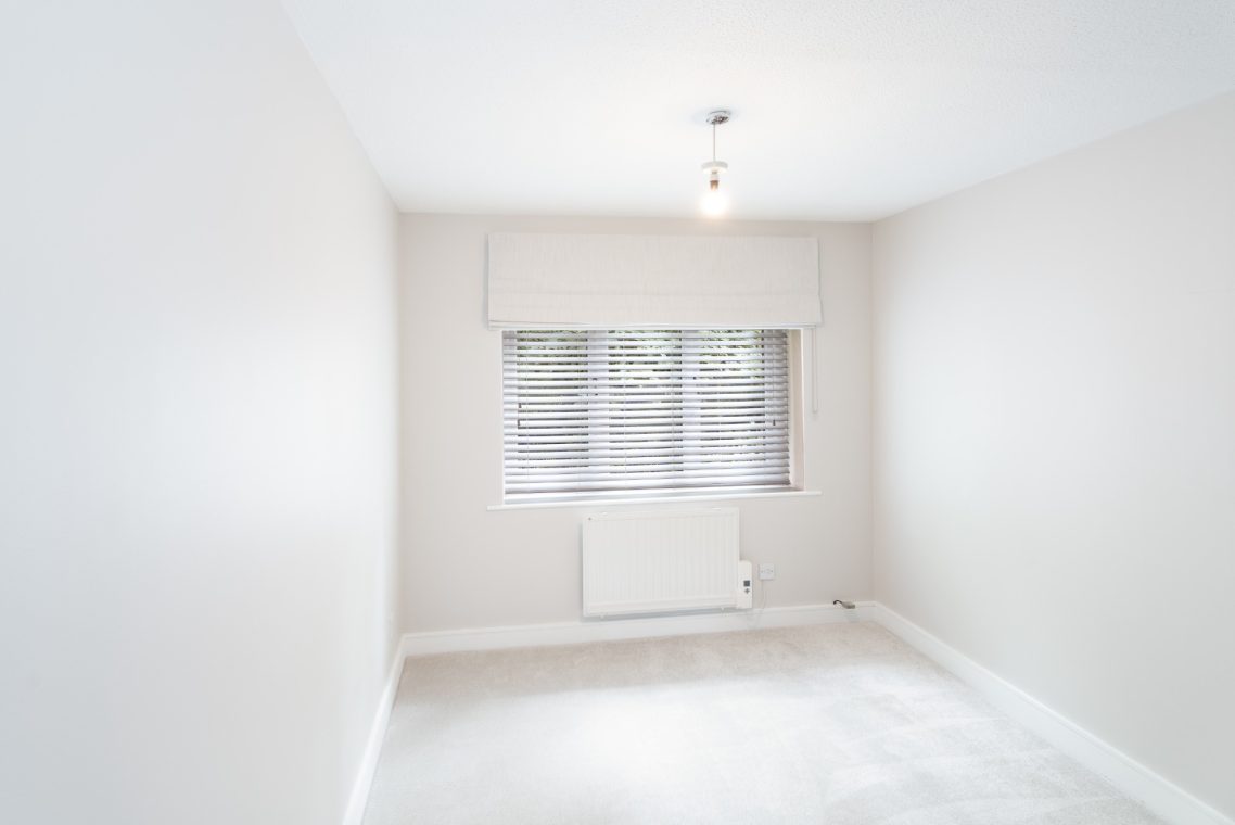 Empty, softly lit room with light walls, a window, and a radiator beneath it.