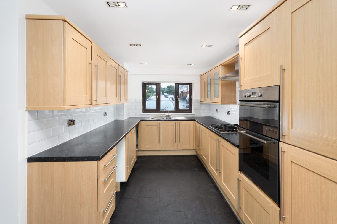 Modern kitchen with wooden cabinetry and dark countertops, featuring built-in appliances.