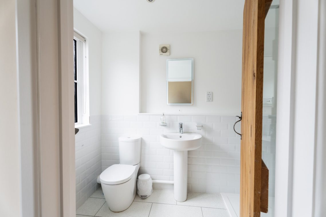 Bright, modern bathroom featuring a toilet, sink, mirror, and tiled floor.