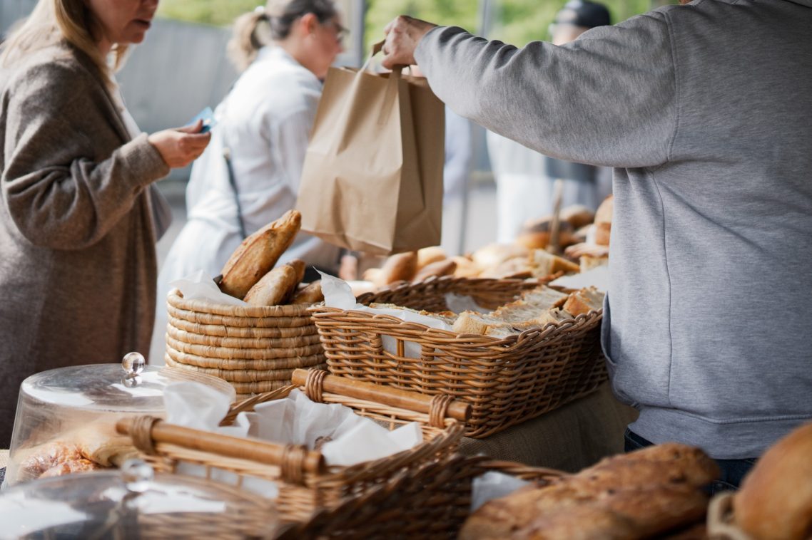 People shopping at a market stall filled with baked goods in baskets.