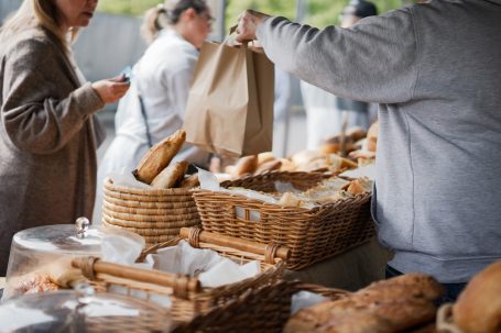 People at a market selecting baked goods from wicker baskets.