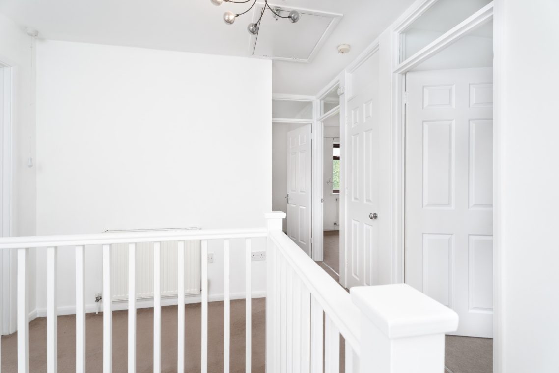Bright hallway with white walls, wooden flooring, and multiple doors leading to different rooms.