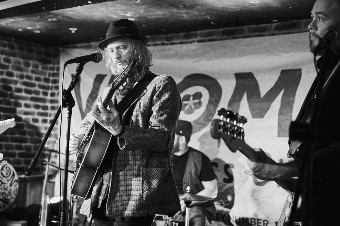 A band performing live on stage in a dimly lit venue.