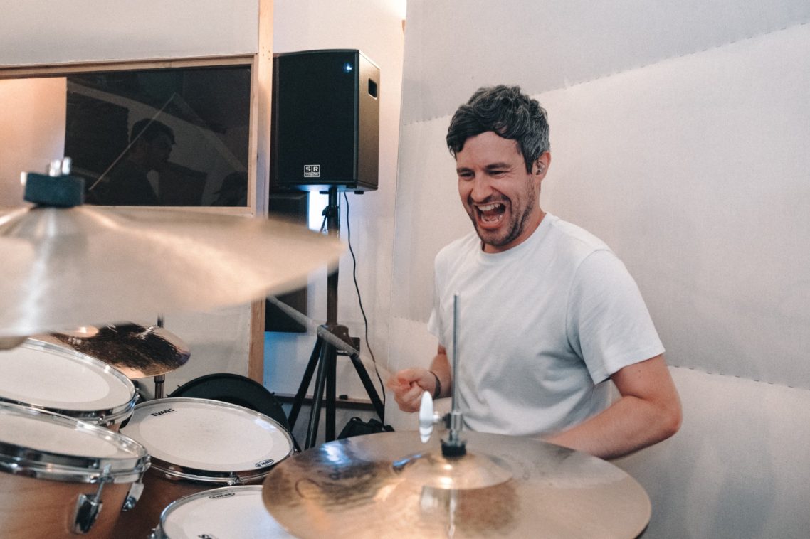 Man playing drums with enthusiasm in a music practice studio.