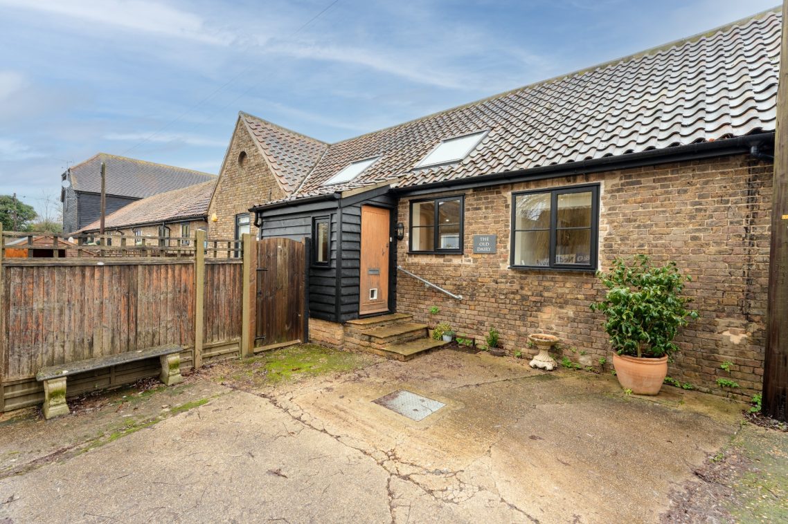 A rustic stone cottage with a black door and potted plants, set in a rural area.