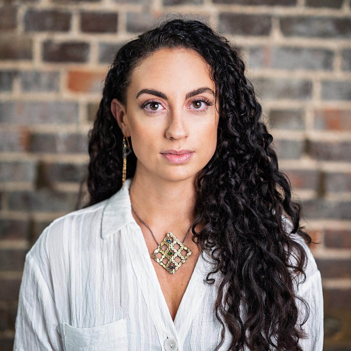 A woman with long curly hair wearing a white shirt and a decorative necklace.