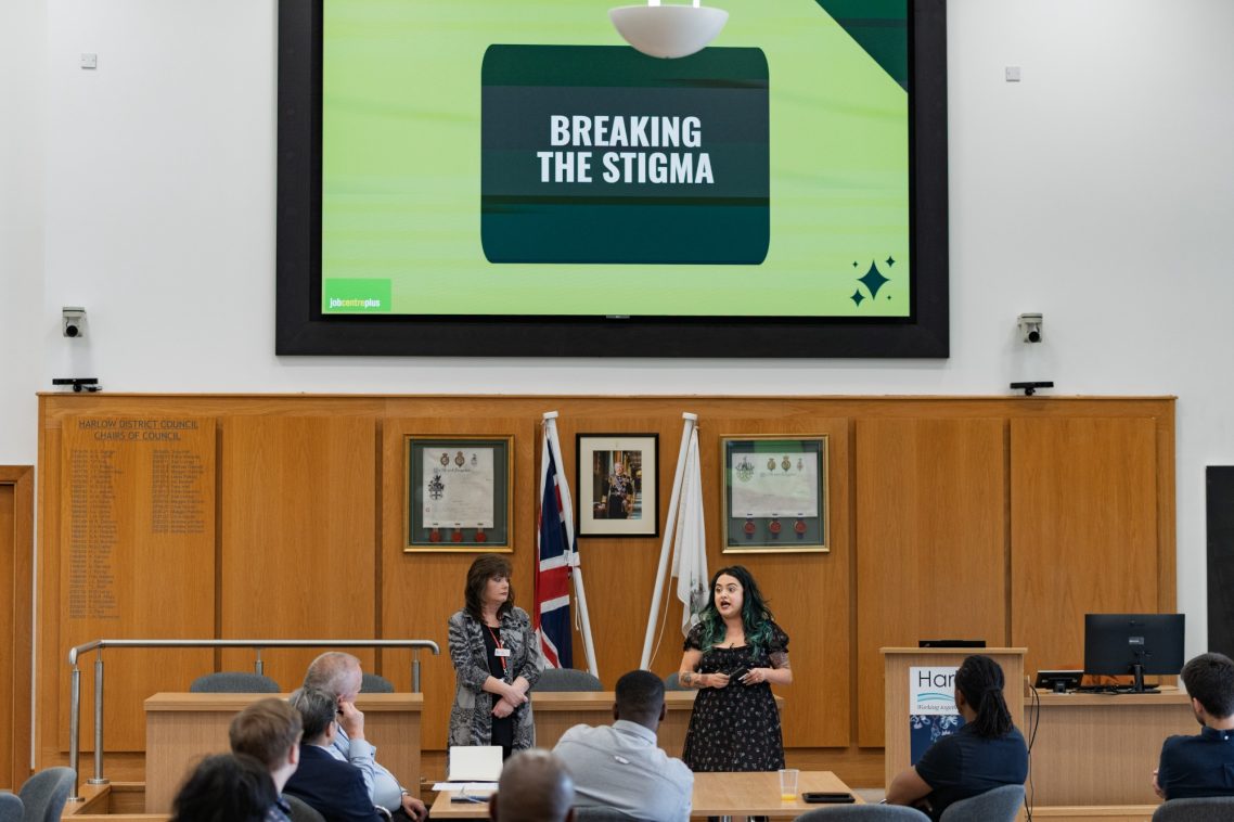 Two speakers present on stage with a "Breaking the Stigma" banner displayed behind them.