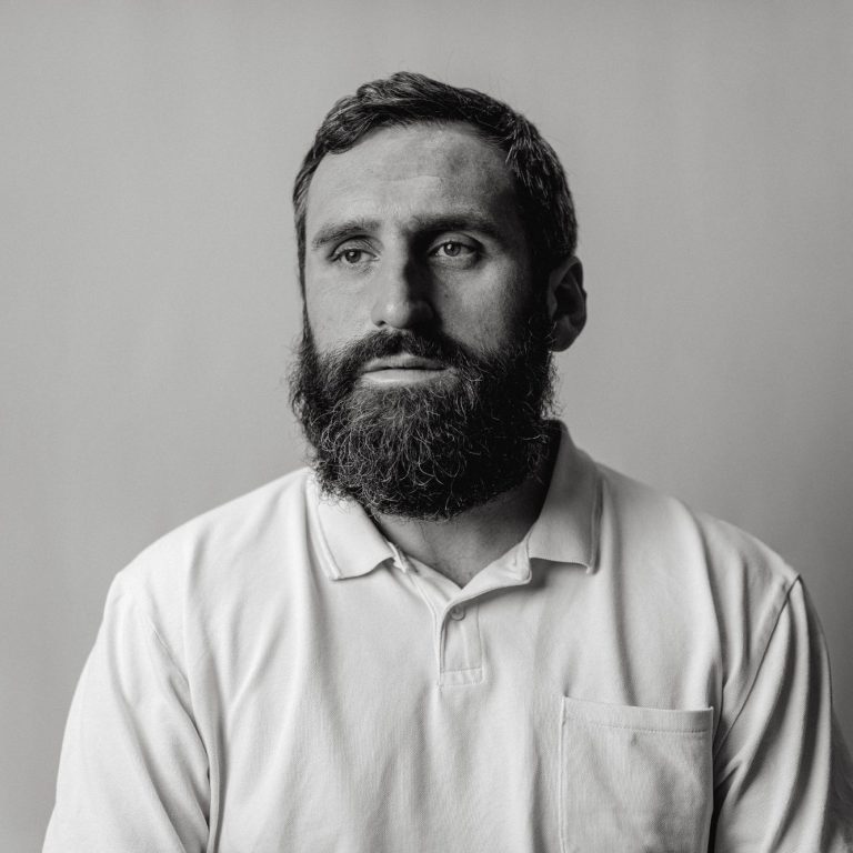 Photograph of a bearded man wearing a polo shirt, looking to one side of the camera.