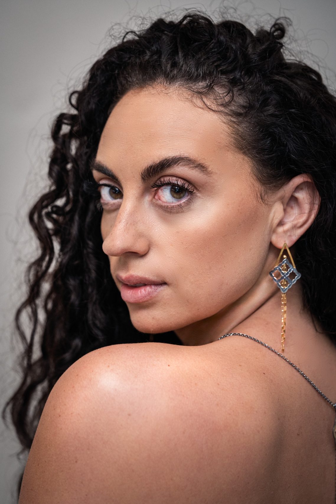 Woman with curly hair and earrings, looking over her shoulder.