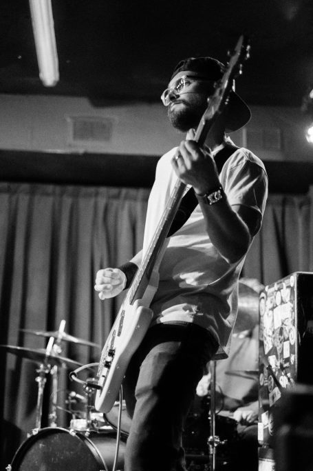 Musician playing bass guitar on stage, focused on performance in black and white.