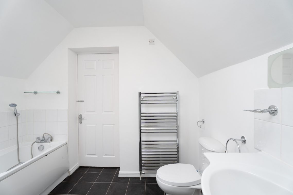 Bright, modern bathroom with a bath, toilet, sink, and towel radiator against white walls.