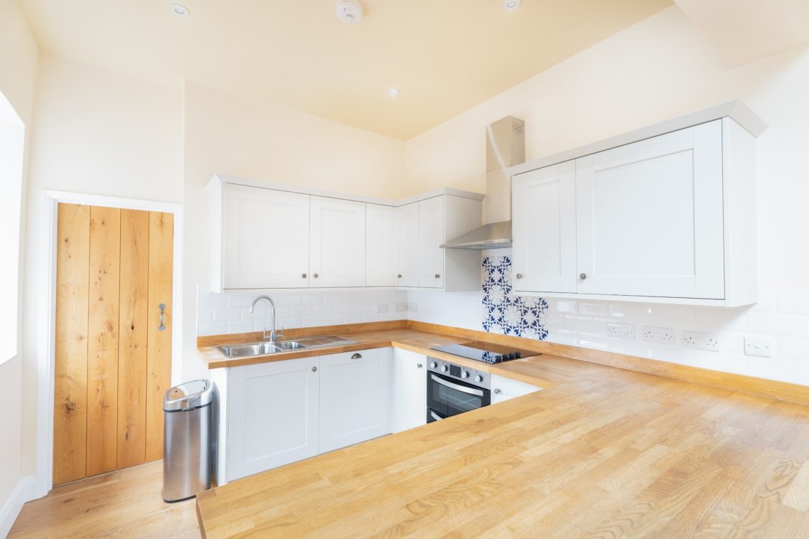 Bright kitchen with wooden countertops, white cabinets, and a blue tiled backsplash.