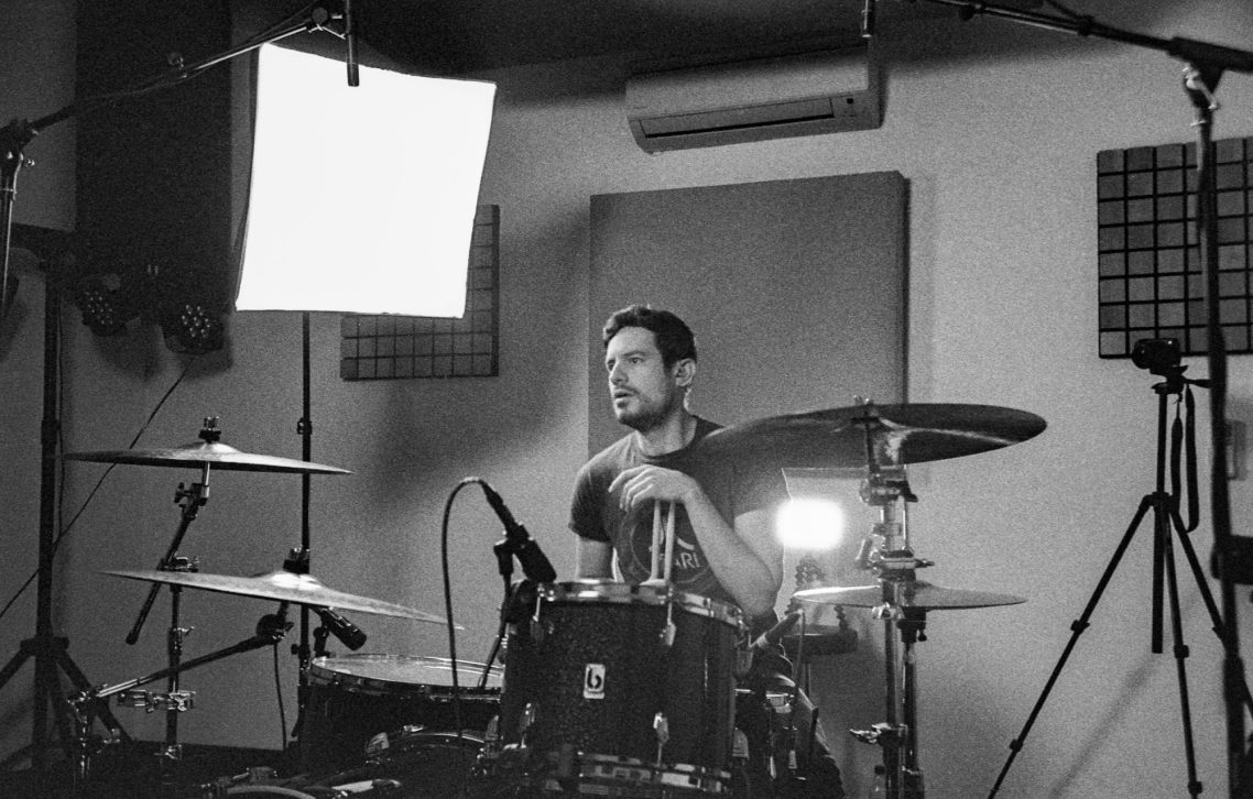 Drummer sitting at a drum kit, focused, in a studio setting with microphones.