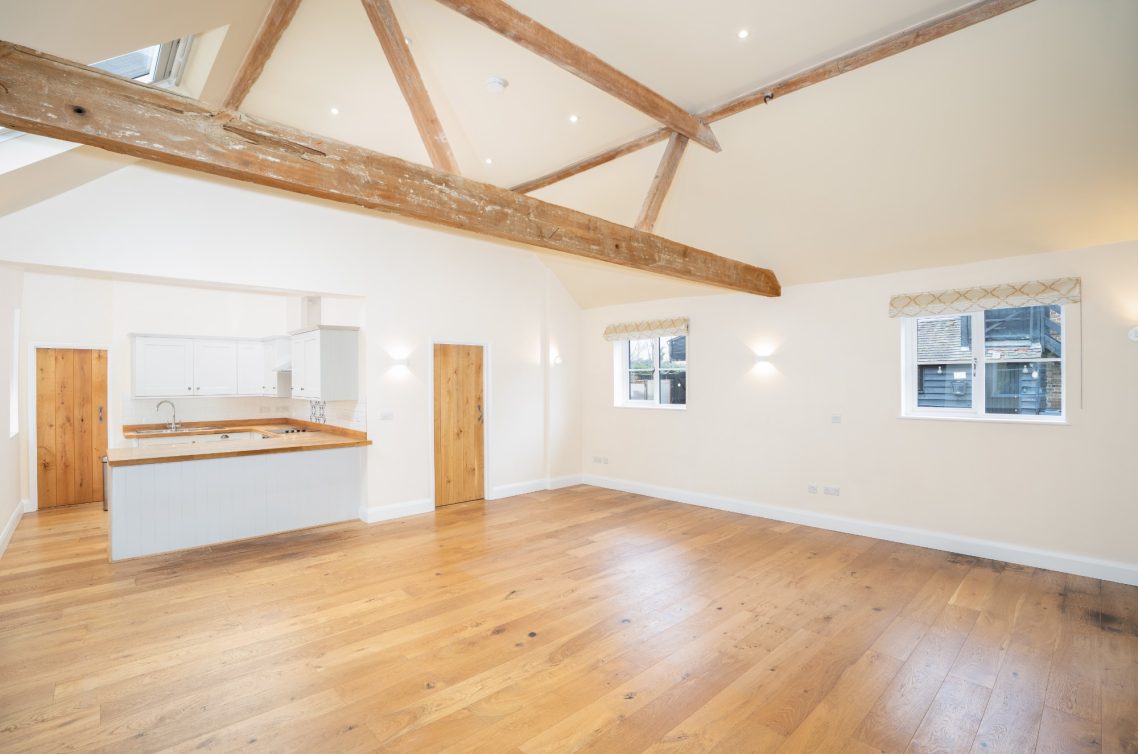 Spacious, airy room with wooden beams and hardwood flooring, featuring a kitchen area.