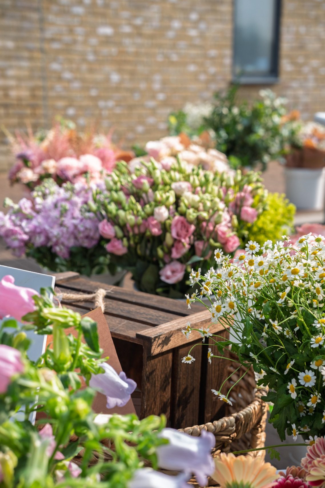 A vibrant arrangement of various flowers in wooden and woven containers.